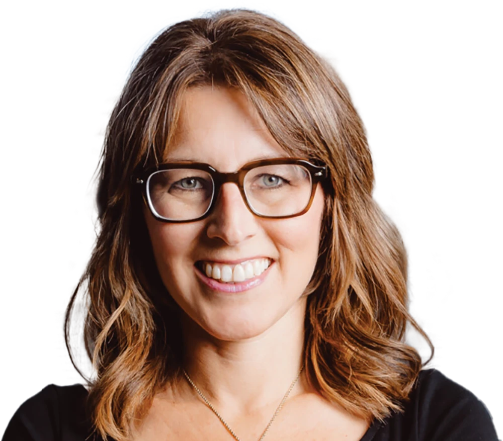 A headshot of a smiling woman with medium-length brown hair, wearing brown-framed glasses and a black shirt.