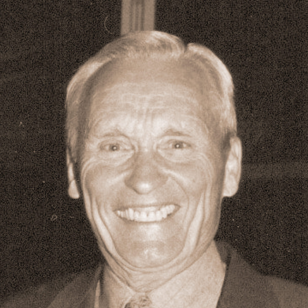 Portrait of an older, smiling white man with light hair and a collared shirt.