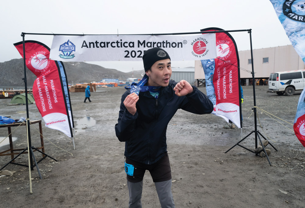 A male runner celebrating at the finish line of the Antarctica Marathon, holding his medal.