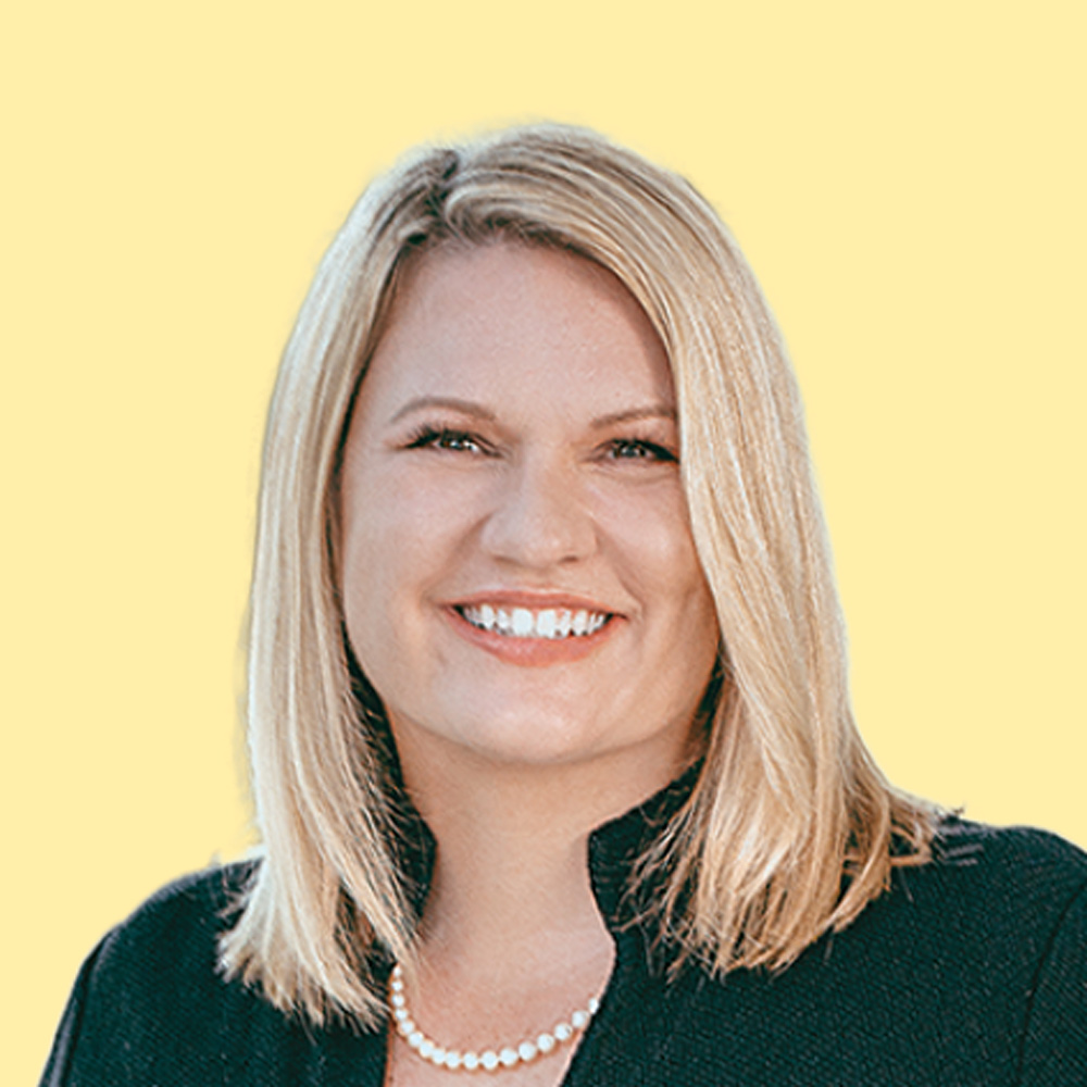 Headshot of a smiling blonde woman wearing a jacket and a pearl necklace against a plain yellow background.