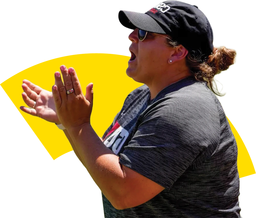 A female coach wearing a black t-shirt and baseball cap claps her hands in support while standing before a yellow graphic.