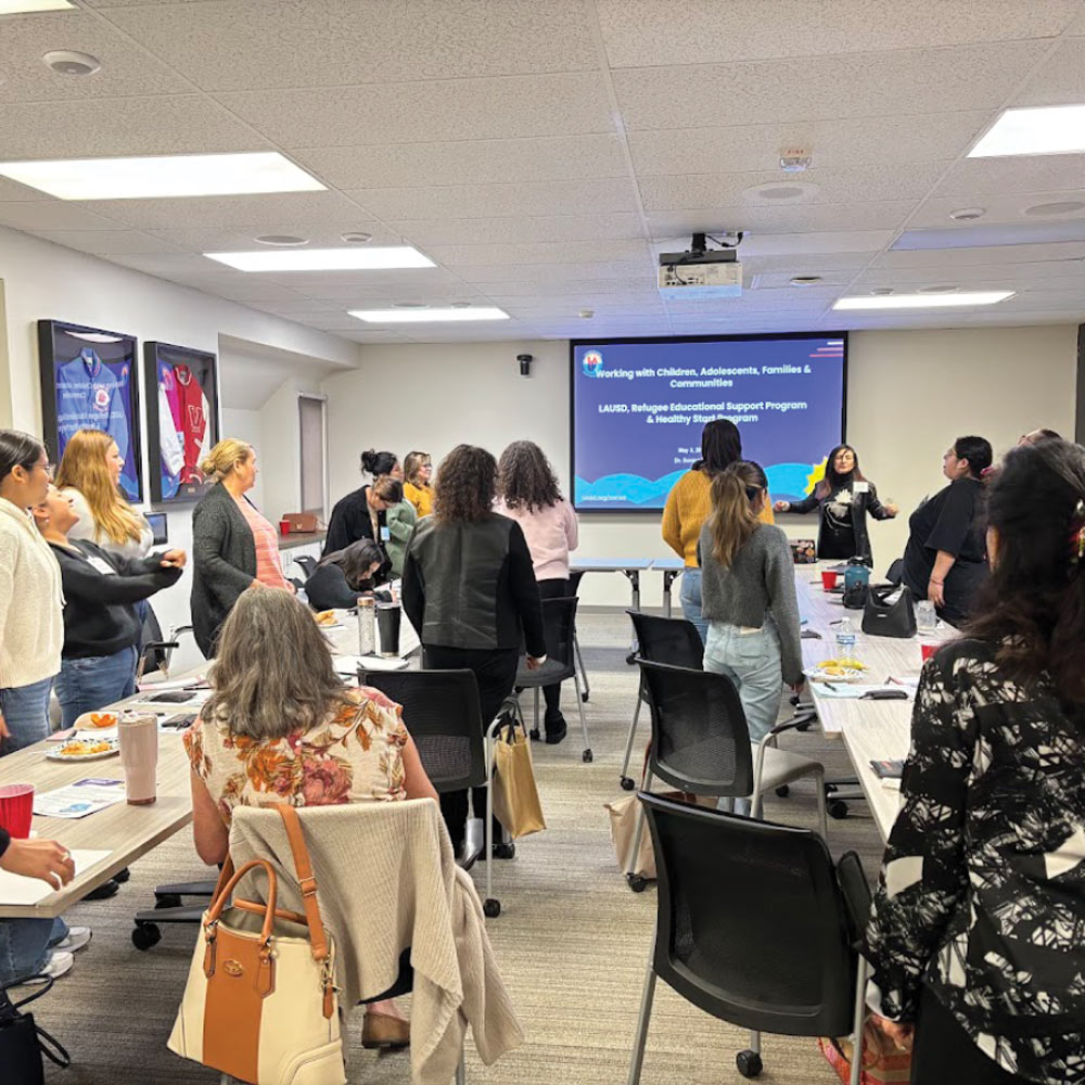 A group of people attending a professional seminar in a conference room with a presentation screen displayed at the front.