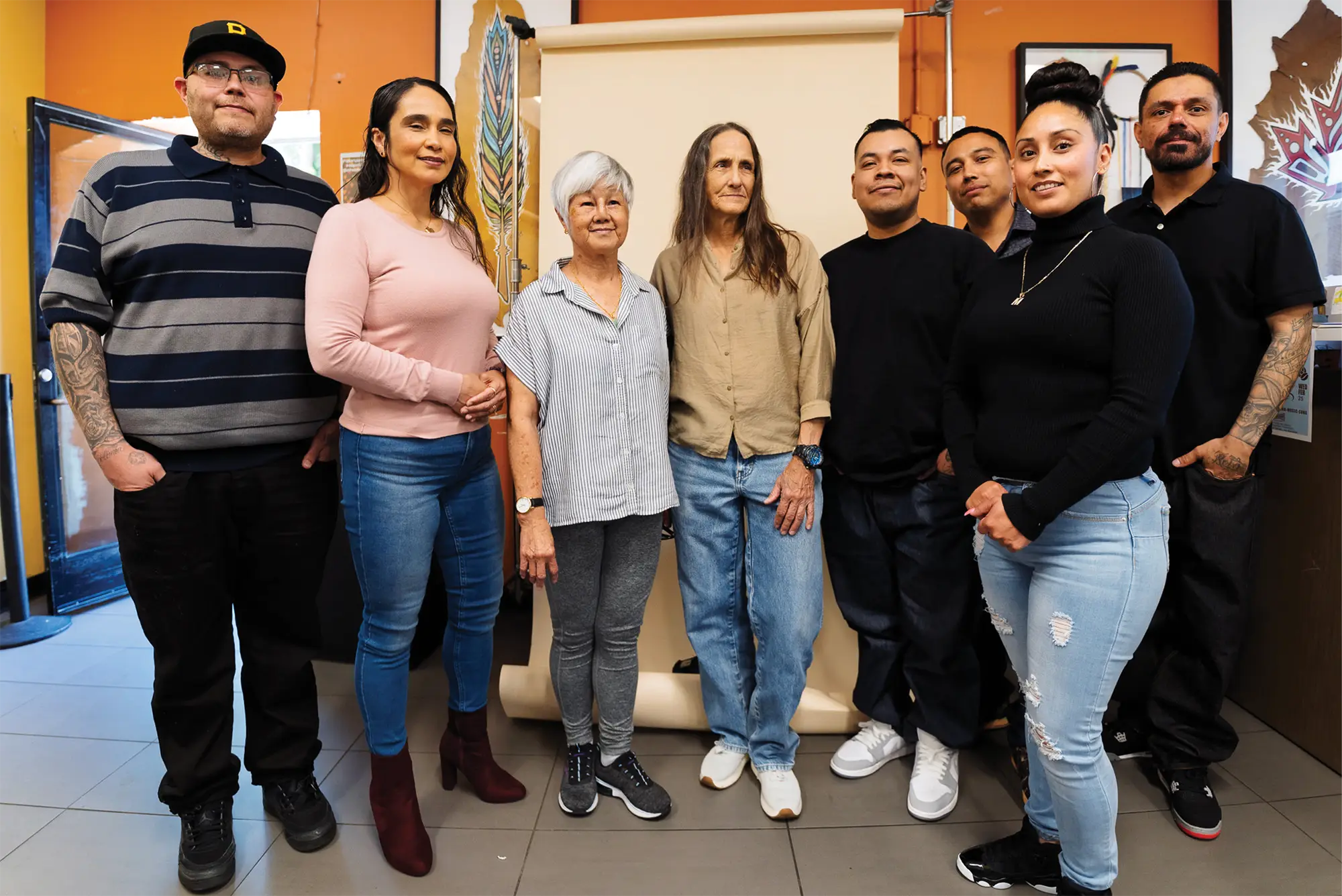 A group of seven people stands together for a portrait in a room with artwork and a photography backdrop.