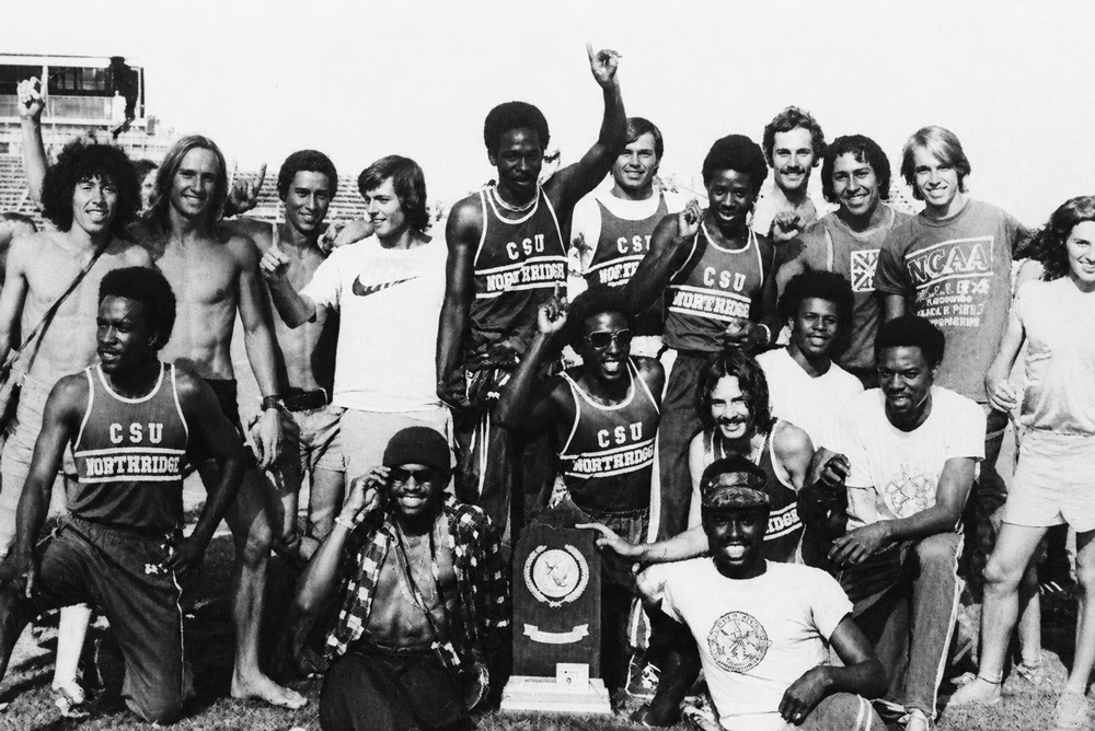 A vintage black-and-white photo of a track team posing together outdoor with a trophy.