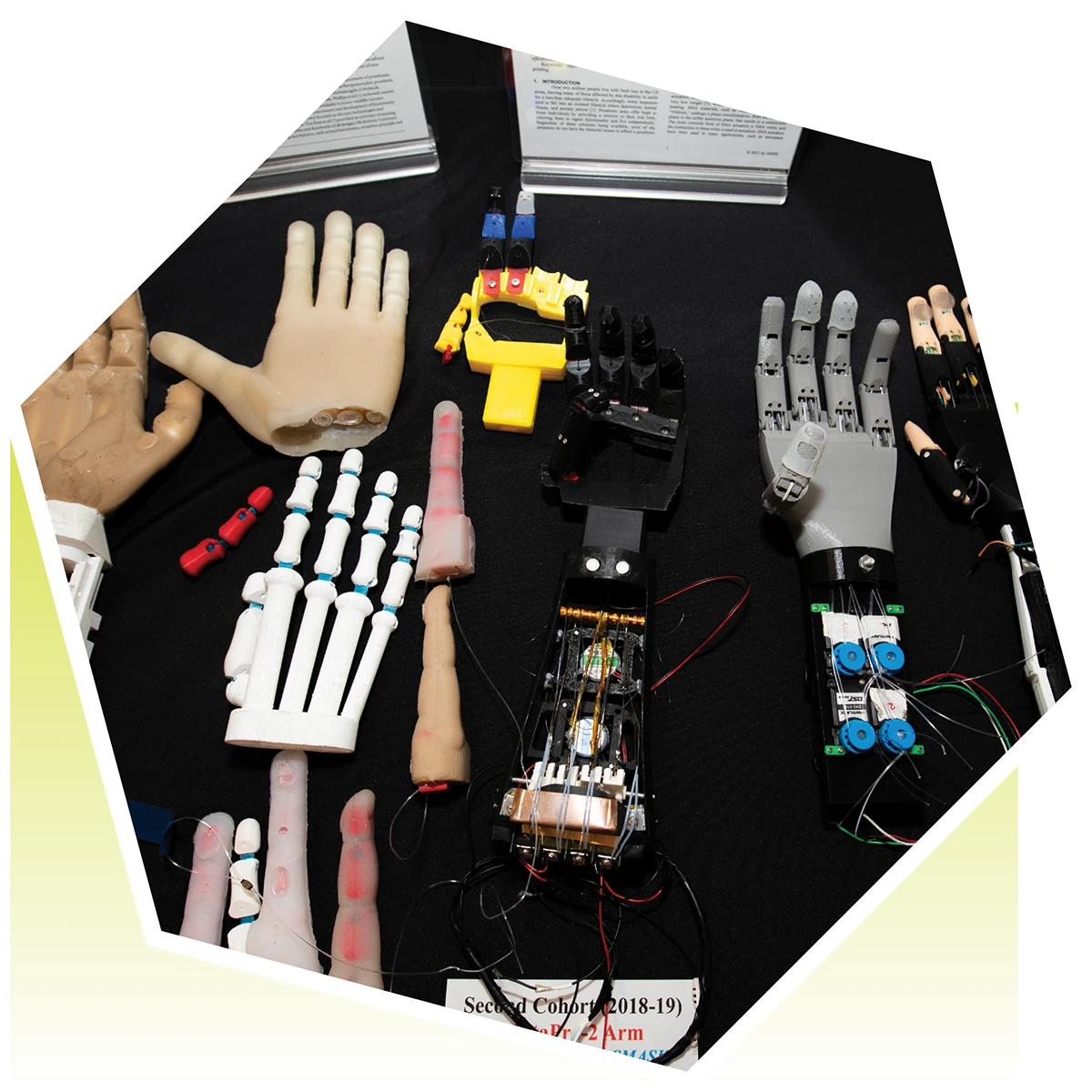 Top-down view of various 3D-printed and mechanical prosthetic hand and arm prototypes displayed on a table.