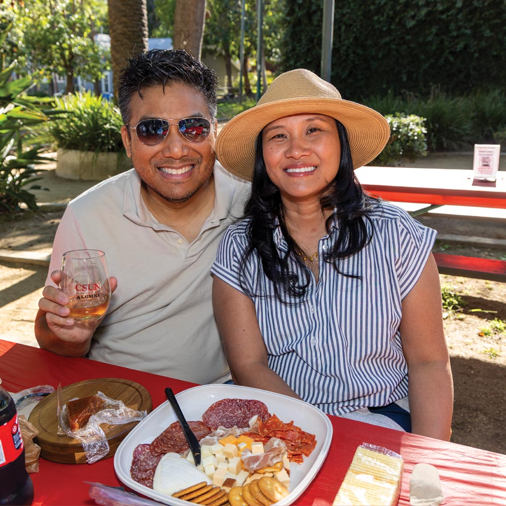 Nick Prampetch and Arwee Parin sitting together at an outdoor picnic table with a charcuterie board and CSUN Alumni glass.