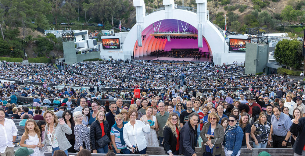 A large crowd of attendees waving from the stands during a concert at the Hollywood Bowl.