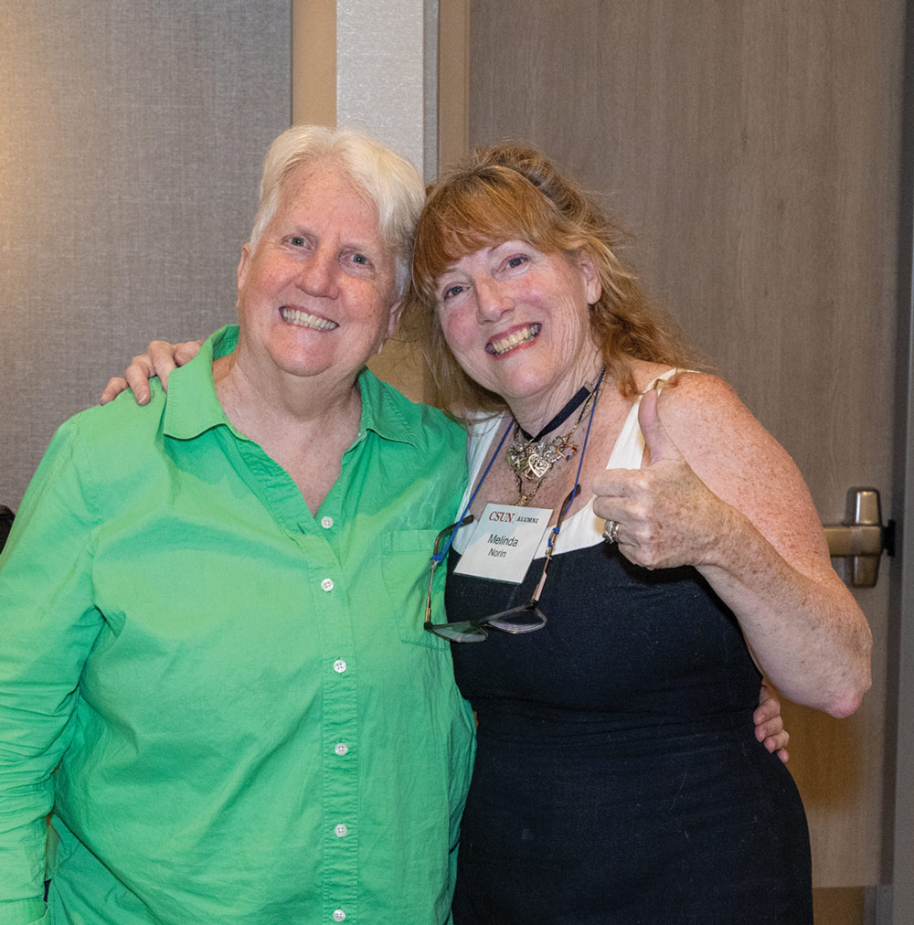 Cathy McLeod and Melinda Norin pose together indoors, with one giving a thumbs-up gesture.
