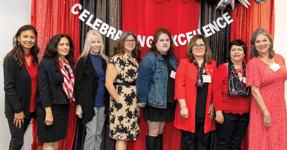 Eight women posing together in front of a red backdrop that reads "Celebrating Excellence."