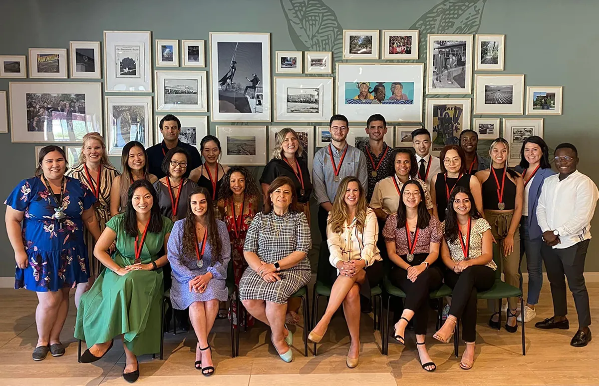 A group of diverse students and faculty posing together indoors in front of a gallery wall with framed photographs.