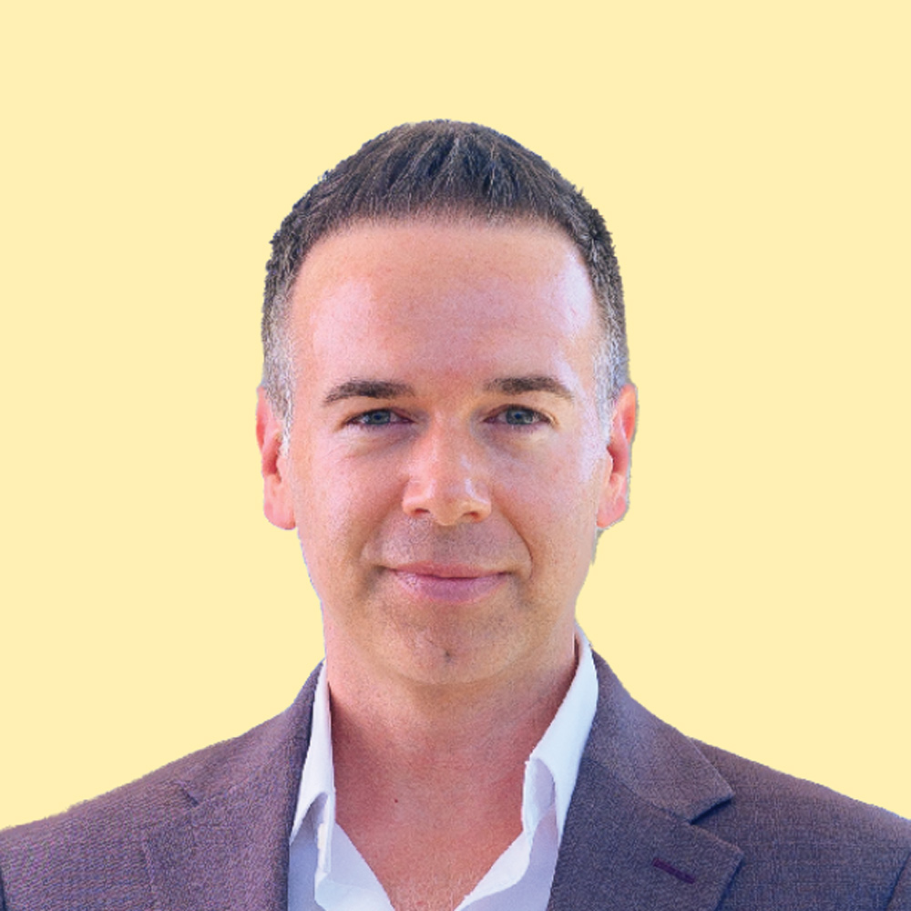 Chad Hilligus in a dark jacket and white collared shirt against a light yellow background.